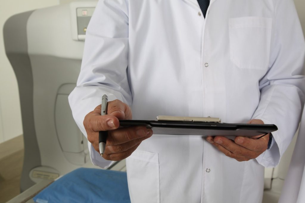 Arzt im weißen Kittel mit Schreibzeug vor dem Tomographen- der Arzt weiß immer, was zu tun ist? 