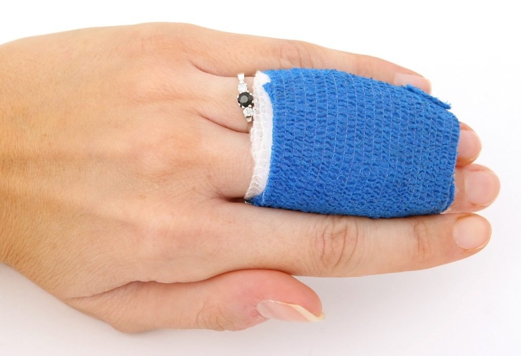 Frauenhand mit Ring und einem Verband um Ring- und MIttelfinger, befestigt mit blauem Tape - Chiron in Verbindung zum Neumond im Widder zeigt uns unsere Verletzlichkeit