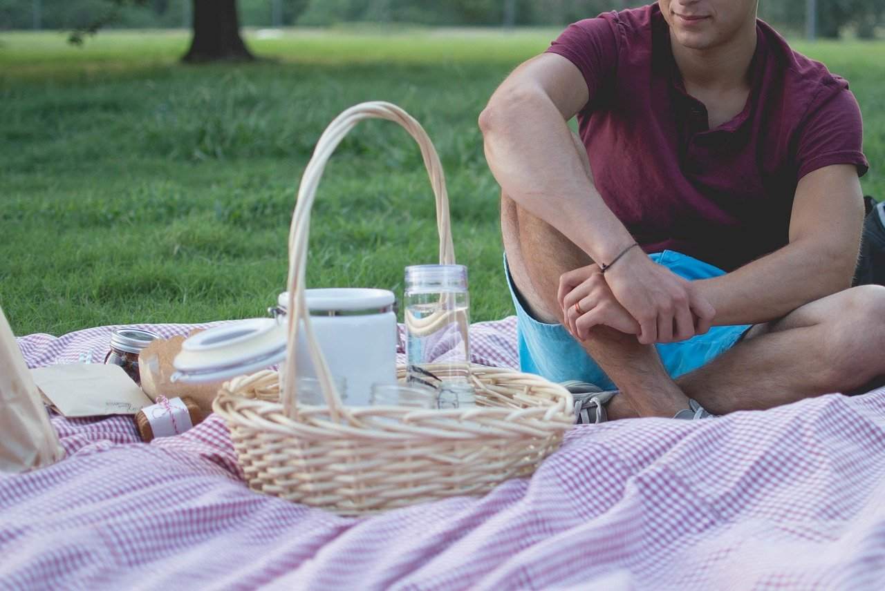 Ein Mann sitzt auf einer Decke auf einer Wiese, Picknick vor ihm ausgebreitet. Sonnenfinsternis im Krebs erinnert uns daran, was für eine Nahrung, auch zwischenmenschlich, wir brauchen. 