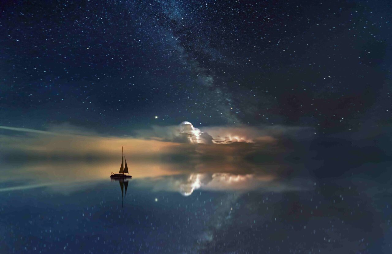 Wasser des Ozeans, in dem sich der Sternenhimmel spiegelt mit einem Segelboot - Jahresthemen 2022, Jupiter-Neptun Konjunktion, Jupiter in Fische