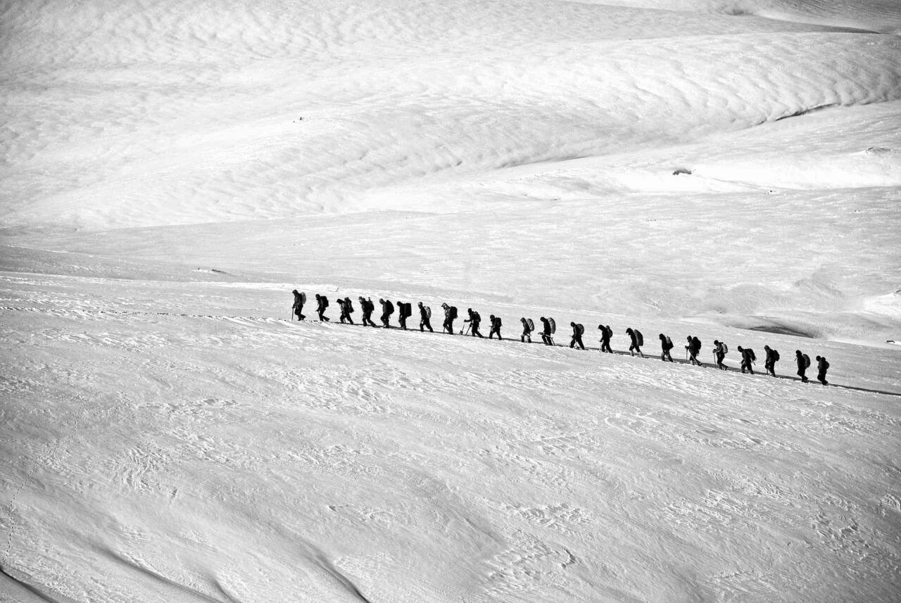 Trekkinggruppe läuft in einer Reihe über ein Schneefeld