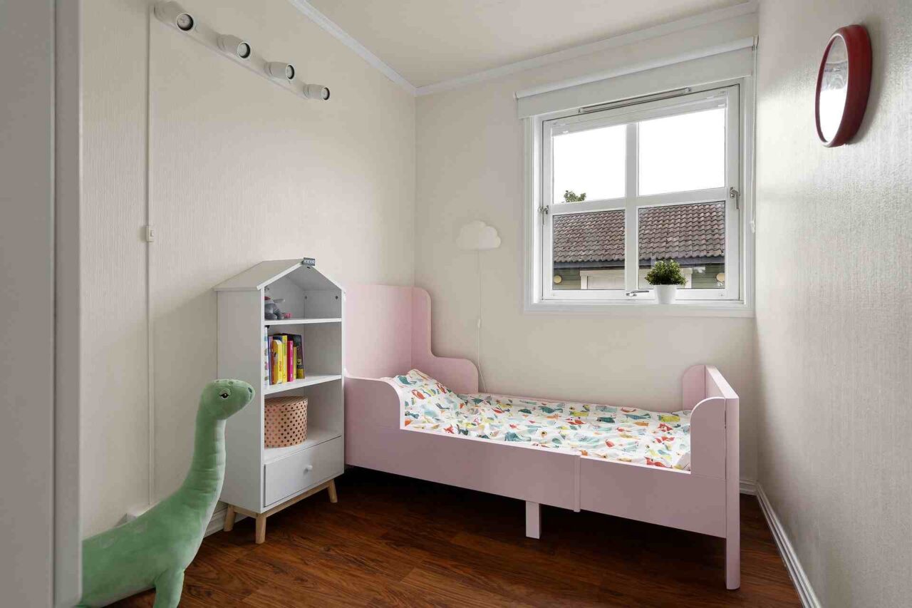 Kinderzimmer mit rosa Bett, einem kleinen Regal und einem großen Drachen aus Samt