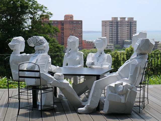 Figuren in weißem Beton sitzen auf Stühlen - die Themen des Mondknoten im Transit sind auf dem Tisch